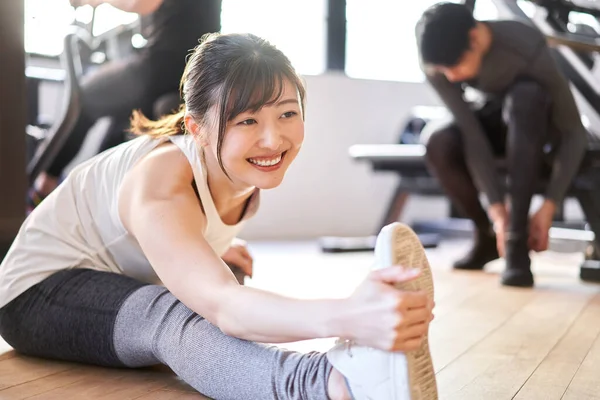 Spor salonunda esneme hareketleri yapan Asyalı bir kadın.
