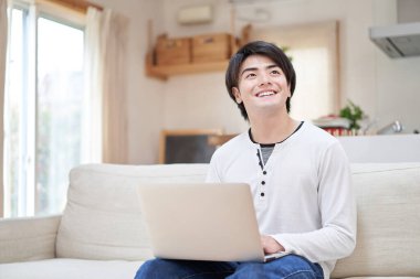 Asyalı bir adam evde bilgisayarla çalışıyor, gülümseyerek.