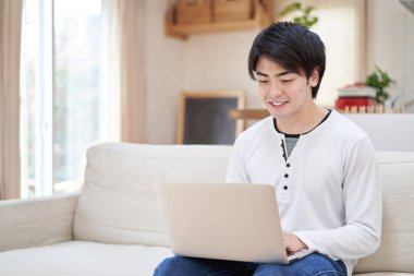 Asyalı bir adam evde bilgisayar üzerinde çalışıyor.