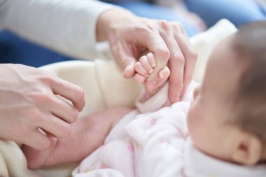 Asyalı bebek babasının parmağını tutuyor.