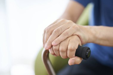 Bastonla oturan yaşlı bir insanın elleri.