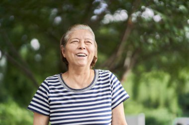 Parkta gülümseyen yaşlı bir kadın.