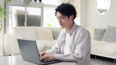 Bilgisayarda çalışırken boynu ağrıyan Asyalı bir adam.