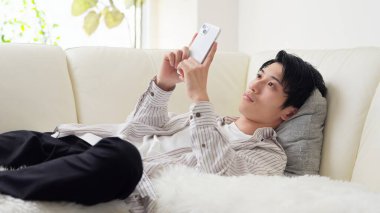 Asyalı bir adam akıllı telefonuna bakarken uyuyakalıyor.