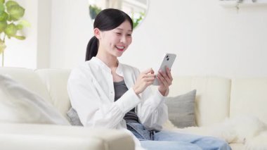 Oturma odasında akıllı telefon kullanan Asyalı kadın.