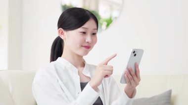 Oturma odasında akıllı telefon kullanan Asyalı kadın.