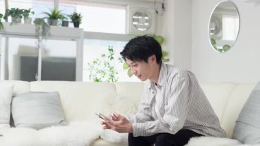 Asyalı adam akıllı telefona bakıyor ve yumruk pompası yapıyor.