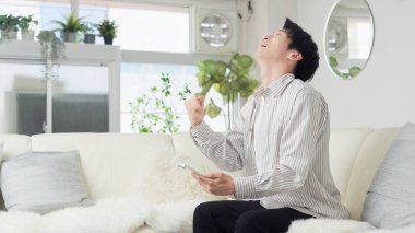 Asyalı adam akıllı telefona bakıyor ve yumruk pompası yapıyor.