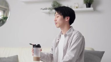 Asyalı adam oturma odasında protein içiyor.