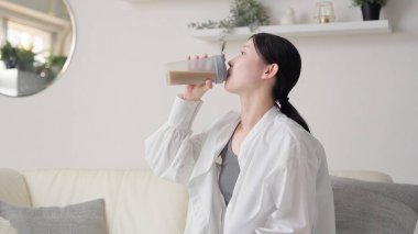 Asyalı kadın oturma odasında protein içiyor.