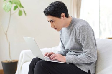 Asyalı bir adam bilgisayar kullanırken eğildi.