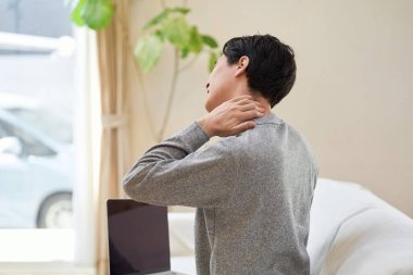 Boynu ağrıyan Asyalı bir adam eline dokunuyor.