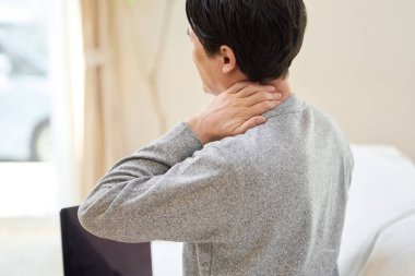 Boynu ağrıyan Asyalı bir adam eline dokunuyor.