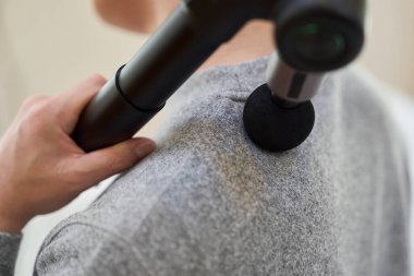 Asyalı bir adam omuzlarında masaj tabancası kullanıyor.