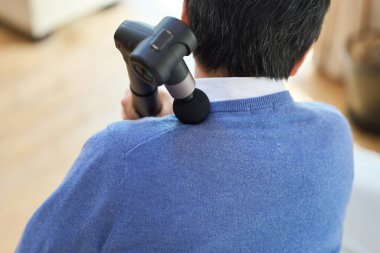 Üst düzey bir Asyalı omuzlarında masaj tabancası kullanıyor.