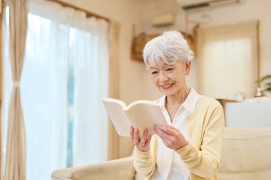 Asyalı son sınıf öğrencisi kadın oturma odasında kitap okuyor.