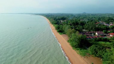 Malezya 'da altın kumu, sakin deniz dalgaları ve yemyeşil evlerle çevrili tropik bir sahil şeridi manzarası..