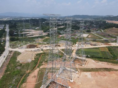 Malezya kırsalındaki yüksek voltaj iletim kulelerinin ve elektrik santrallerinin havadan ve yerden görünüşü, enerji altyapısı ve güç dağıtım ağını gösteriyor.