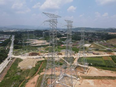 Malezya kırsalındaki yüksek voltaj iletim kulelerinin ve elektrik santrallerinin havadan ve yerden görünüşü, enerji altyapısı ve güç dağıtım ağını gösteriyor.
