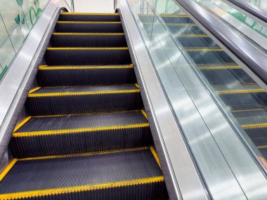 Bir alışveriş merkezindeki yürüyen merdivende güvenlik işaretleri ve yukarıdan görülen sarı basamaklar var..