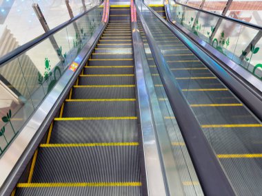 Bir alışveriş merkezindeki yürüyen merdivende güvenlik işaretleri ve yukarıdan görülen sarı basamaklar var..