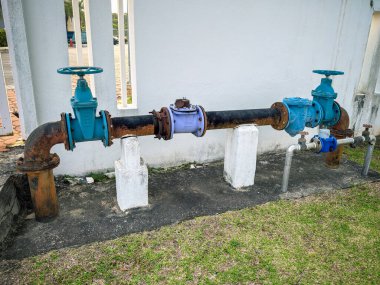 Dış binanın yanında beton desteklere bağlı vanalar ve eklemlerle korunmasız bir su boru hattı sistemi..