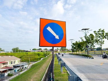 Bir yol kenarı trafik levhası beyaz aşağı doğru ok ile mavi bir daire gösteriyor, araçların takip etmesi gereken yönü gösteriyor..