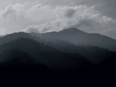 Moody black-and-white landscape of layered mountains fading into mist under dramatic cloudy skies.
