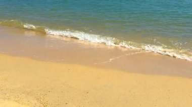 Yumuşak dalgalar açık mavi gökyüzünün altında uzak bir adayla kumlu bir sahile vuruyor..