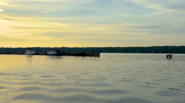 Gün batımında iskeleye yanaşmış teknelerle ve suya yansıyan altın ışıkla sakin bir rıhtım sahnesi..