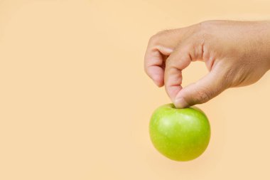 Pastel arka planda yeşil bir elma tutarak sağlıklı beslenme, beslenme seçimi, sağlıklı yaşam tarzı ve temiz gıda kavramını temsil ediyor..