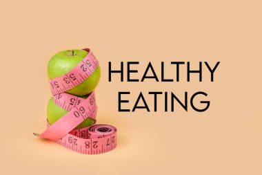 Tahta blokların yanında pembe bir mezura ile sarılmış yeşil elmalar diyet, kilo kaybı, kalori kontrolü, sağlıklı beslenme ve sağlıklı yaşam tarzı kavramlarını sembolize ediyor..