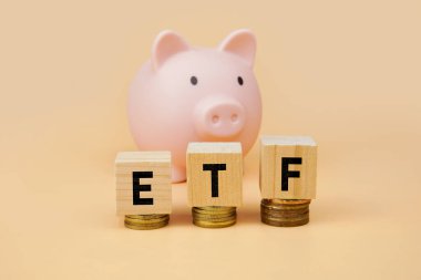 ETF yatırım kavramı, domuz kumbarasının önündeki istiflenmiş paraların üzerine tahta bloklar konarak, çeşitli portföyleri, pasif yatırımları ve uzun vadeli finansal büyümeyi sembolize ediyor.