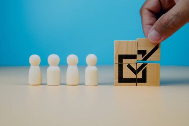 Çalışan değerlendirmesi ve performans kontrolü konsepti. Görev tamamlama, kalite kontrolü, değerlendirme, KPI incelemesi ve takım yönetimini temsil eden işaretli sembollü ahşap blokların elle birleştirilmesi.