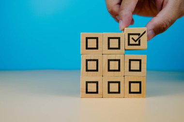 Görev tamamlama ve karar verme konsepti. Tahta bloklar üzerinde bir onay kutusu seçmek, verimliliği, iş akışı yönetimini, öncelik ayarını, onayını ve başarılı proje uygulamasını sembolize etmek.