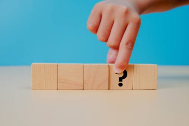 Karar verme ve problem çözme kavramı. Mavi arka planda soru işareti olan tahta küpün elle seçilmesi, seçimi, belirsizliği, analizi, stratejiyi, düşünme sürecini ve iş kararlarını temsil eder.