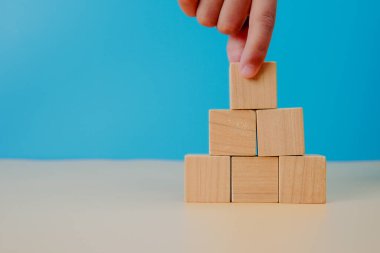 Business growth and strategy concept. Hand stacking wooden cubes into pyramid shape, symbolizing planning, development, progress, stability, and building a strong foundation for success.