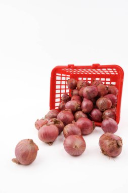 Plastik sepetten dökülen kırmızı soğanlar beyaz arka planda izole edilmiş taze pazar ürünlerini, yiyecek kaynaklarını ve günlük yemek malzemelerini temsil ediyor..