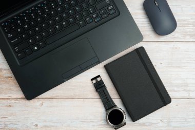 Üst görünüm iş alanı dizüstü bilgisayarı, fare, not defteri ve beyaz ahşap masa üzerindeki kol saati üretkenliği, zaman yönetimini, dijital çalışmayı ve temiz kopya alanı olan profesyonel ofis düzeneğini temsil ediyor..