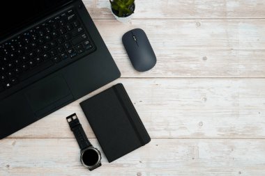 Üst görünüm iş alanı dizüstü bilgisayarı, fare, not defteri ve beyaz ahşap masa üzerindeki kol saati üretkenliği, zaman yönetimini, dijital çalışmayı ve temiz kopya alanı olan profesyonel ofis düzeneğini temsil ediyor..