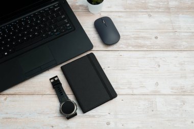 Üst görünüm iş alanı dizüstü bilgisayarı, fare, not defteri ve beyaz ahşap masa üzerindeki kol saati üretkenliği, zaman yönetimini, dijital çalışmayı ve temiz kopya alanı olan profesyonel ofis düzeneğini temsil ediyor..