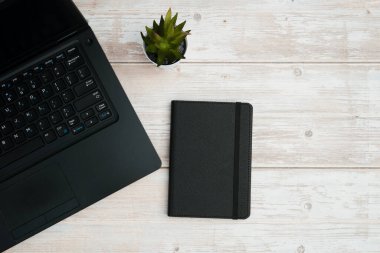 Verimliliği, planlamayı, dijital çalışma ortamını ve temiz fotokopi alanı olan profesyonel ofis ortamını temsil eden dizüstü bilgisayarlı, defterli ve beyaz ahşap masa üzerindeki işletme çalışma alanının en üst görünümü.