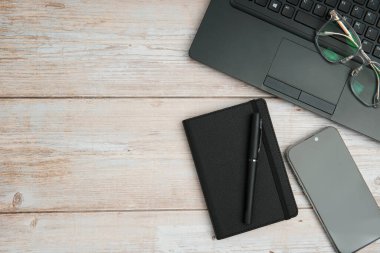 Üst görünüm iş alanı dizüstü bilgisayarı, gözlükleri, defteri ve beyaz ahşap masadaki akıllı telefonu ile verimliliği, dijital çalışmayı, planlamayı ve temiz kopya alanı olan profesyonel ofis kurulumunu temsil ediyor..