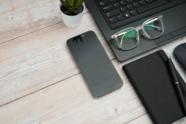 Dizüstü bilgisayarlı, akıllı telefonlu, gözlüklü, defterli ve fareli en iyi iş yeri beyaz ahşap masadaki verimliliği, dijital çalışmayı ve temiz kopya alanı olan profesyonel ofis ortamını temsil ediyor..