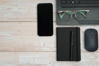 Dizüstü bilgisayarlı, akıllı telefonlu, gözlüklü, defterli ve fareli en iyi iş yeri beyaz ahşap masadaki verimliliği, dijital çalışmayı ve temiz kopya alanı olan profesyonel ofis ortamını temsil ediyor..