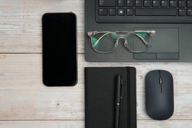 Dizüstü bilgisayarlı, akıllı telefonlu, gözlüklü, defterli ve fareli en iyi iş yeri beyaz ahşap masadaki verimliliği, dijital çalışmayı ve temiz kopya alanı olan profesyonel ofis ortamını temsil ediyor..