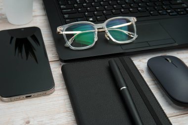 Dizüstü bilgisayarlı, akıllı telefonlu, gözlüklü, defterli ve fareli en iyi iş yeri beyaz ahşap masadaki verimliliği, dijital çalışmayı ve temiz kopya alanı olan profesyonel ofis ortamını temsil ediyor..