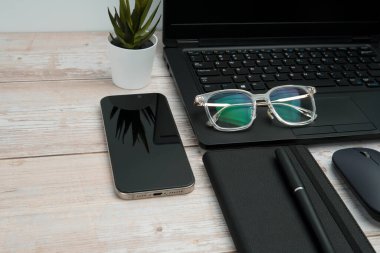 Dizüstü bilgisayarlı, akıllı telefonlu, gözlüklü, defterli ve fareli en iyi iş yeri beyaz ahşap masadaki verimliliği, dijital çalışmayı ve temiz kopya alanı olan profesyonel ofis ortamını temsil ediyor..