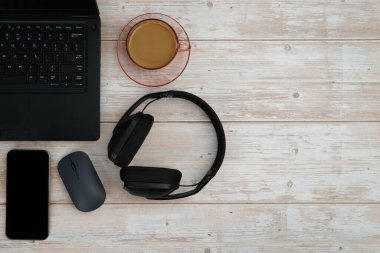 Bilgisayarlı, akıllı telefonlu, fareli, kulaklıklı ve beyaz ahşap masadaki kahve ile en üst düzey çalışma alanı üretkenliği, uzaktan çalışmayı, dijital odağı ve temiz kopya alanı olan profesyonel ofis ortamını temsil ediyor..