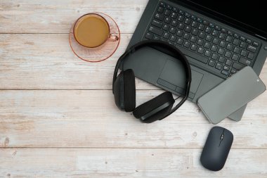 Bilgisayarlı, akıllı telefonlu, fareli, kulaklıklı ve beyaz ahşap masadaki kahve ile en üst düzey çalışma alanı üretkenliği, uzaktan çalışmayı, dijital odağı ve temiz kopya alanı olan profesyonel ofis ortamını temsil ediyor..